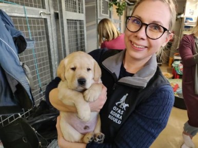 A smilling Hannele holds a yellow lab puppy